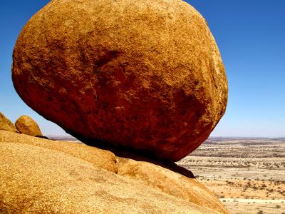 Giant boulder perched on the edge of a bluff overlooking a desert landscape