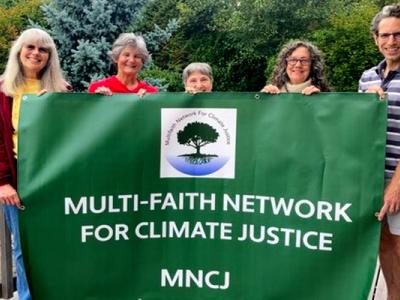 Members of the Multi-Faith Network for Climate Justice proudly hold a large green banner for their organization.